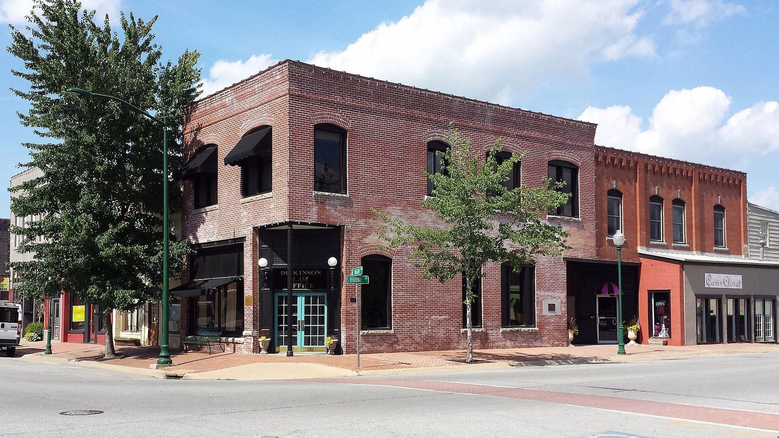 Two-story red brick Harkness Building on a sunny day in downtown Siloam Springs, Arkansas, with shade trees and a wide sidewalk out front