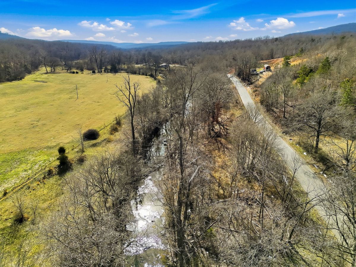 Drone view down a creek valley in Adair County, Oklahoma, with open pasture on one side and a county road on the other